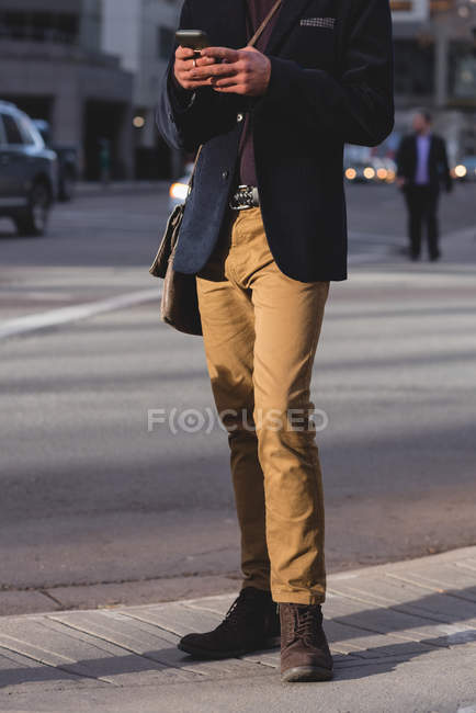 Sección baja del hombre usando el teléfono móvil mientras camina por la calle - foto de stock