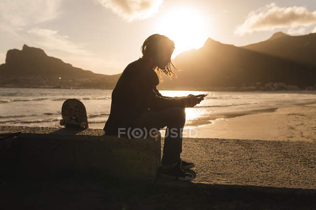 Silueta del hombre usando el teléfono móvil en la playa - foto de stock