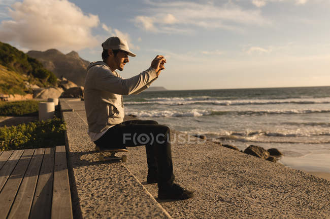 Seitenansicht eines Mannes, der mit dem Handy auf ein Foto am Strand klickt — Stockfoto
