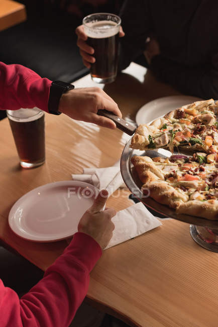 Man taking slice of pizza from tray in pub — Stock Photo