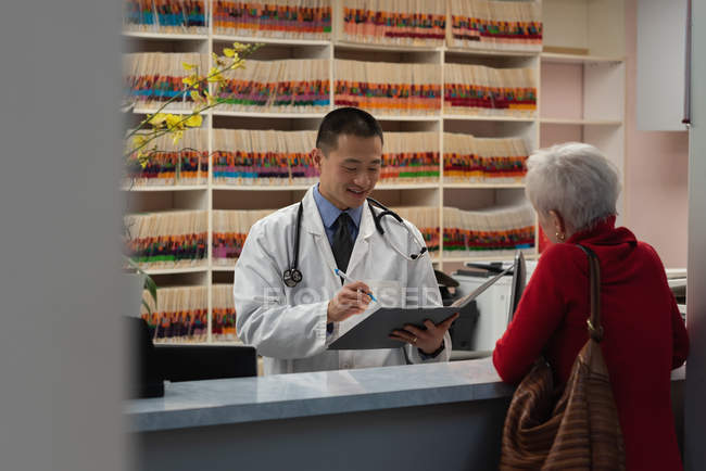 Vista frontal del joven médico asiático que prescribe medicamentos para el paciente en la clínica - foto de stock