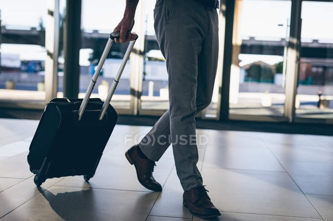 Low-section of a businessman walking with his travel suitcase in the office — Stock Photo