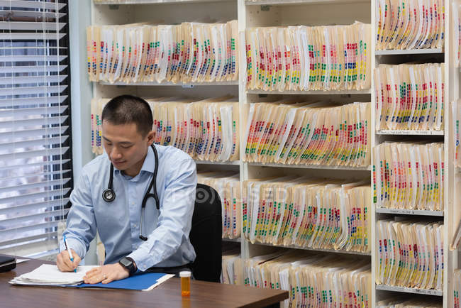Visão frontal de yong asain médico masculino prescrevendo medicina no relatório na clínica — Fotografia de Stock