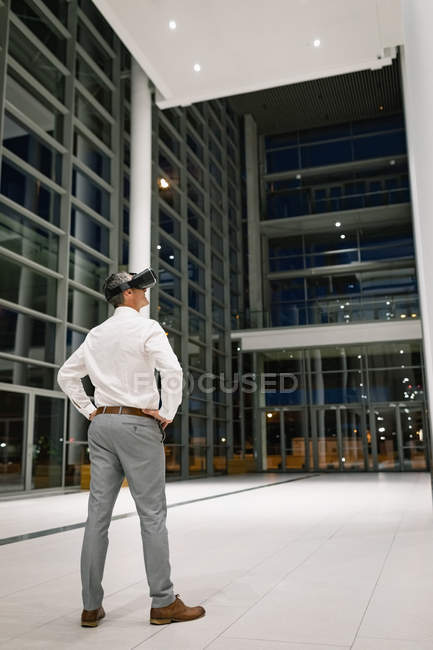 Rear view of businessman experiencing VR headset outside the office by night — Stock Photo