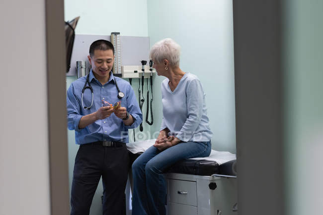 Giovane asiatico maschio medico e anziano paziente discutere oltre orecchio modello a clinica — Foto stock
