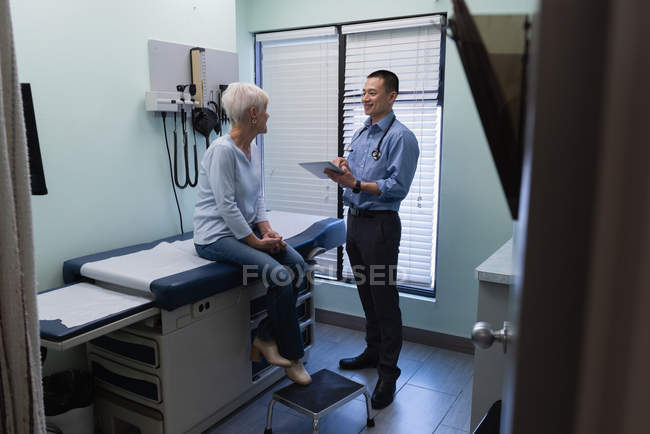Вид сбоку на молодого врача-азиата и пожилого пациента, взаимодействующего друг с другом в клинике — стоковое фото
