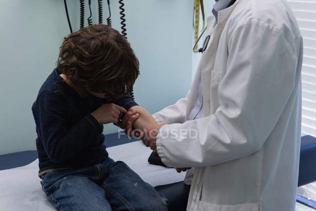 Средняя часть молодого азиатского врача мужского пола проверяет кровяное давление пациента кавказского мальчика в клинике — стоковое фото