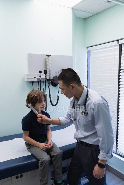 Vista lateral de joven asiático médico masculino mostrando tenedor de sintonía a caucásico niño paciente en clínica - foto de stock