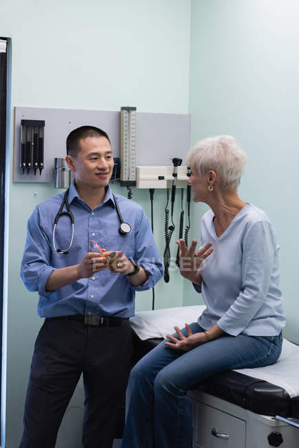 Молодой врач-азиат и пожилой пациент обсуждают модель сердца в клинике — стоковое фото
