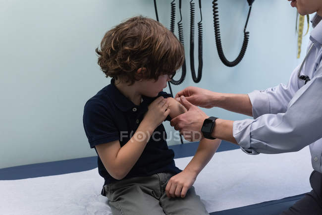 Вид сбоку на молодого врача-азиата, вводящего шприц кавказскому мальчику в клинику — стоковое фото