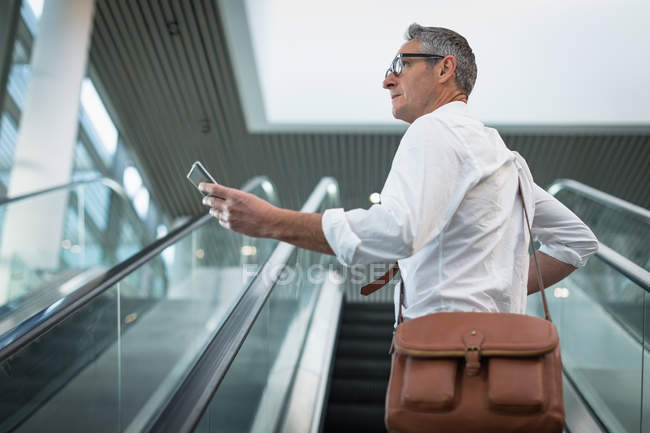 Вид збоку бізнесмена, який перевіряє свій мобільний телефон на ескалаторі в офісі — стокове фото