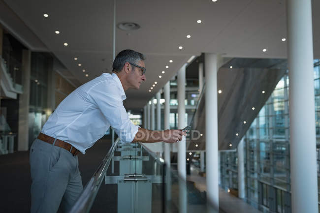 Side view of thoughtful businessman with his phone leaning on the railings in office — Stock Photo
