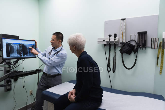 Задний план молодого азиатского врача-мужчины, обсуждающего рентгеновский отчет на компьютере в клинике — стоковое фото