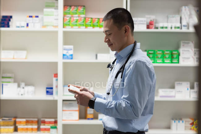 Vista laterale del giovane medico maschio asiatico che tiene la medicina e in piedi in clinica — Foto stock