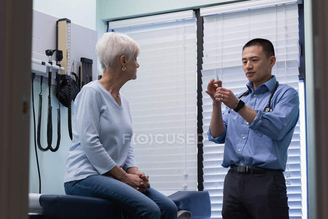 Jovem Asiático médico masculino injetando paciente sênior na clínica — Fotografia de Stock