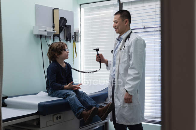 Vista lateral de joven asiático médico masculino hablando con chico en clínica - foto de stock