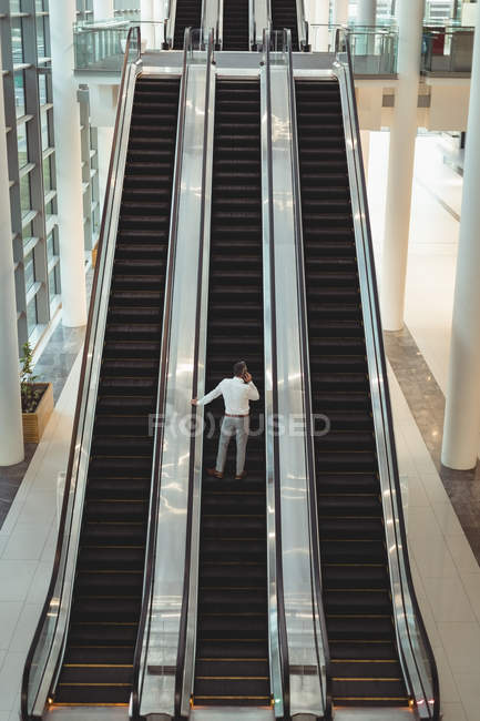 Erhabener Blick auf Geschäftsmann, der auf Rolltreppe im Büro mit seinem Handy spricht — Stockfoto