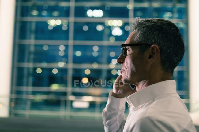 Vue latérale rapprochée d'un homme d'affaires parlant au téléphone devant un immeuble de bureaux la nuit — Photo de stock