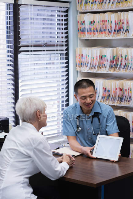 Frontansicht eines jungen asiatischen Arztes und eines älteren Patienten im Gespräch über ein digitales Tablet in der Klinik — Stockfoto