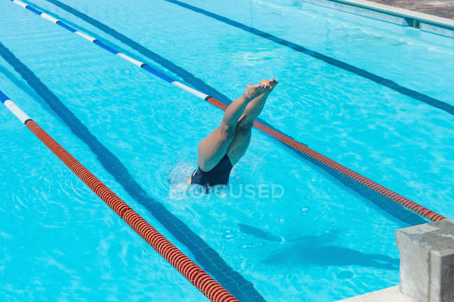 Vista alta da jovem nadadora caucasiana pulando na água de uma piscina ao sol — Fotografia de Stock