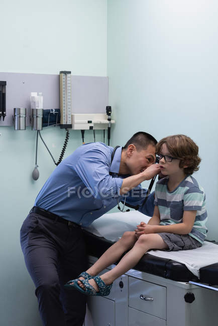 Vue latérale de jeune asiatique mâle médecin examen caucasien garçon patient avec outil dans une clinique — Photo de stock