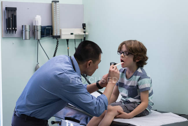 Side view of young asian male doctor examining caucasian boy patient with tool in a clinic — Stock Photo