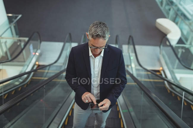 High of businessman using his mobile phone on the escalator in office — Stock Photo