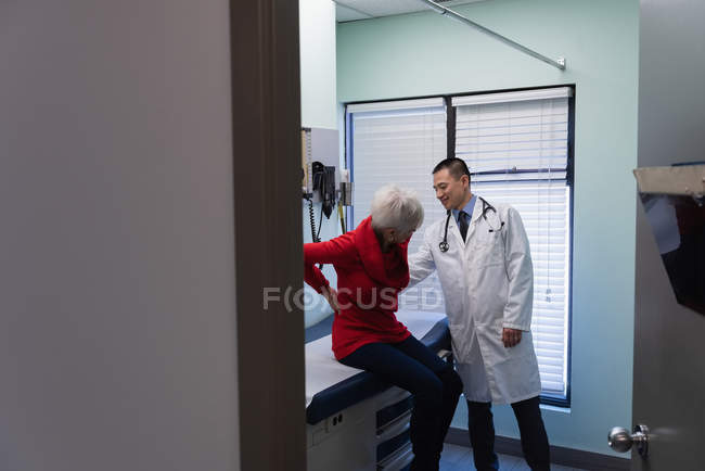 Молодий азіатський лікар перевіряє задню кістку старшої пацієнтки в клініці — стокове фото