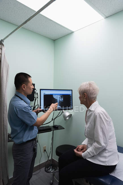 Вид збоку молоді азіатські чоловічого доктора обговорювати над рентгенівського доповідь на комп'ютері в клініці — стокове фото