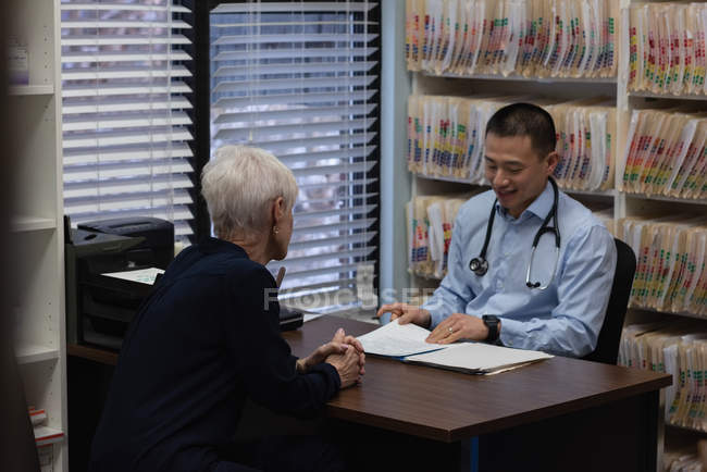 Young Asian male doctor and senior patient interacting with each other at clinic — Stock Photo