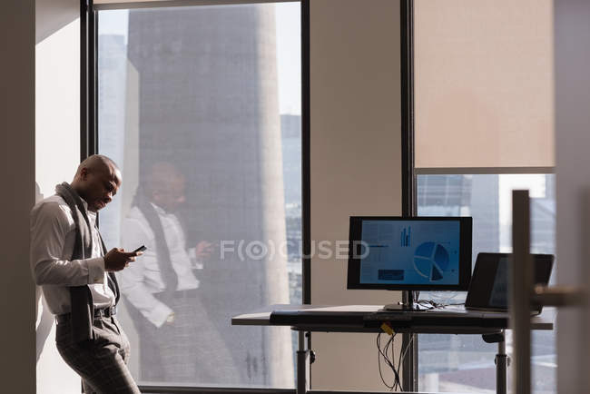 Vista lateral do empresário de pé usando telefone celular no escritório moderno — Fotografia de Stock