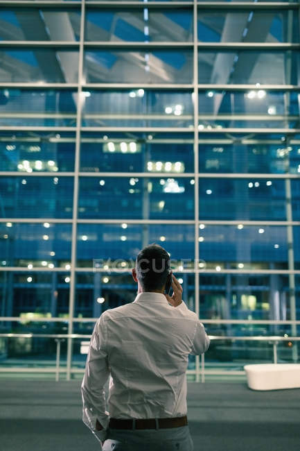 Visão traseira do empresário falando ao telefone do lado de fora de um prédio de escritórios à noite — Fotografia de Stock