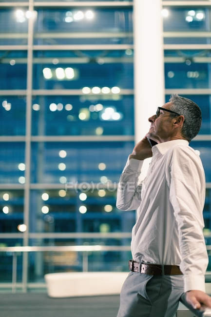 Side view of businessman talking on the phone outside a office building by night — Stock Photo