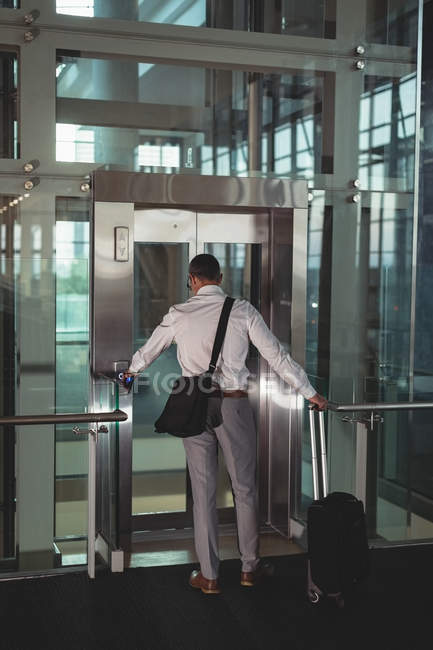 Вид ззаду бізнесмена з дорожньою сумкою, що викликає ліфт в офісі — стокове фото