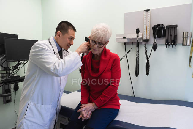 Первый взгляд на молодого азиатского врача, осматривающего старшего пациента в клинике — стоковое фото
