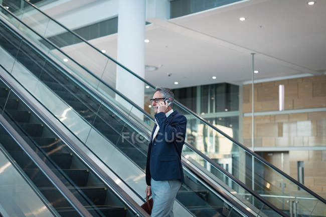 Vue latérale de l'homme d'affaires parlant sur le téléphone mobile sur l'escalator dans le bureau — Photo de stock