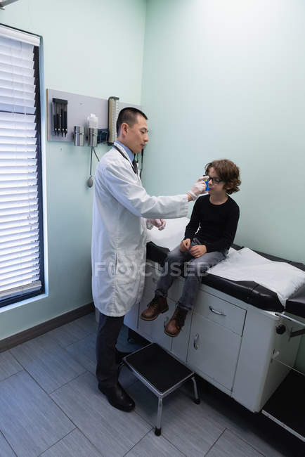 Jovem asiático médico masculino ajudando um menino caucasiano paciente no uso de inalador de asma na clínica — Fotografia de Stock