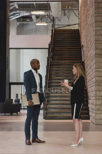 Бічний погляд на ділових людей, що взаємодіють один з одним, стоячи у вестибюлі в сучасному офісі — стокове фото
