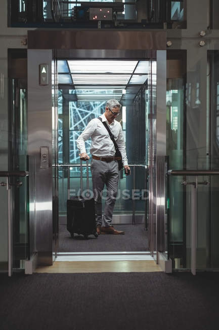 Vista frontal de un hombre de negocios con maleta de viaje esperando en el ascensor en la oficina - foto de stock