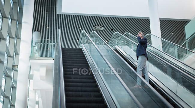 Low view of businessman talking on the mobile phone on escalator in office — Stock Photo
