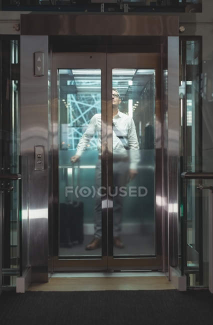 Vista frontale di un uomo d'affari con valigia da viaggio in ascensore in ufficio — Foto stock