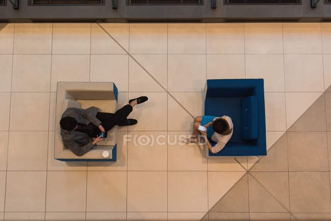 Vista superior de la gente de negocios usando el teléfono móvil sentado en los sillones modernos en el vestíbulo en la oficina - foto de stock