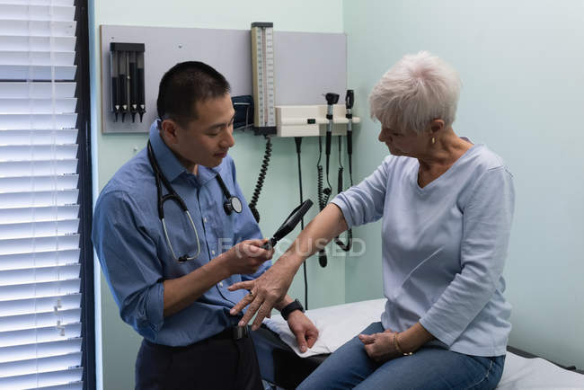 Vorderansicht eines jungen asiatischen männlichen Arztes bei der Untersuchung eines älteren Patienten mit Lupe in der Klinik — Stockfoto