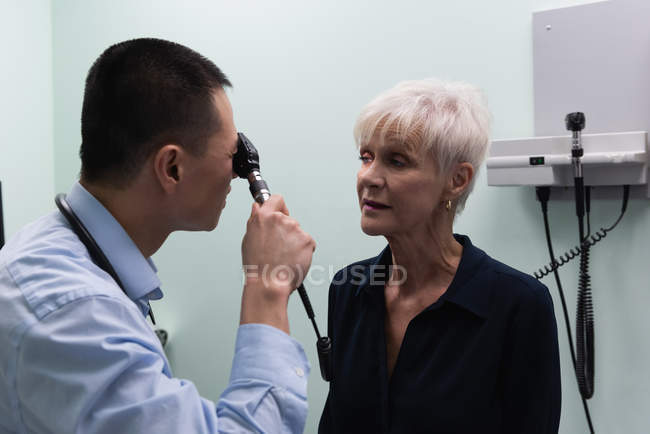 Primer plano del joven médico asiático examinando a un paciente mayor en la clínica - foto de stock