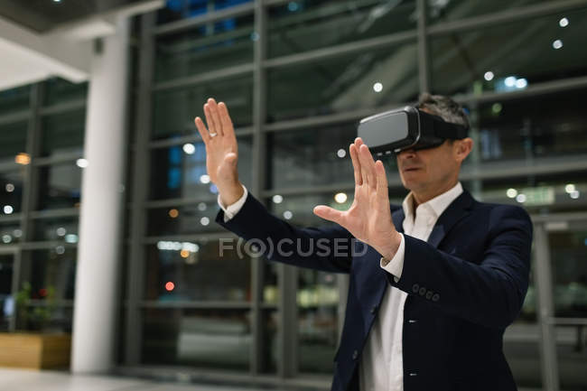 Vista frontal de un hombre de negocios que experimenta auriculares VR y levanta las manos fuera de la oficina por la noche - foto de stock