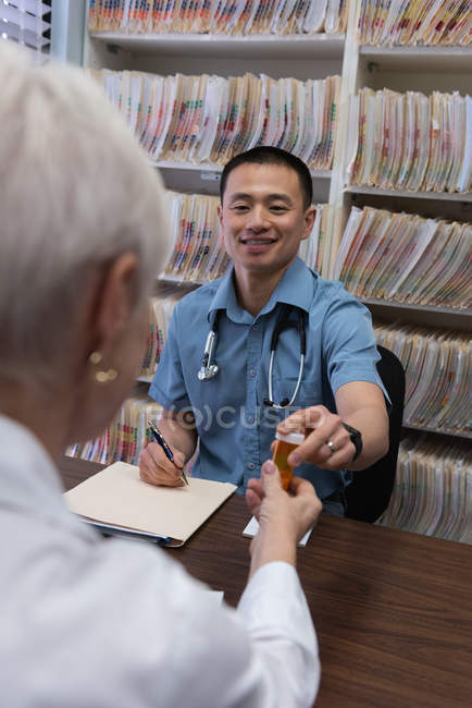 Vista frontal de un joven médico asiático y un paciente mayor interactuando entre sí en la clínica - foto de stock