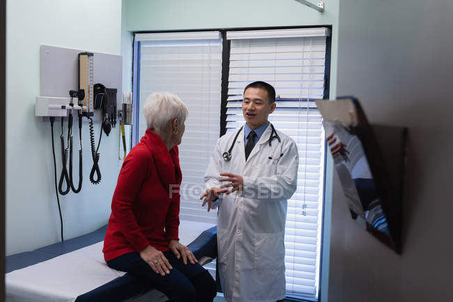 Vorderansicht eines jungen asiatischen Arztes, der mit einem älteren Patienten in der Klinik interagiert — Stockfoto