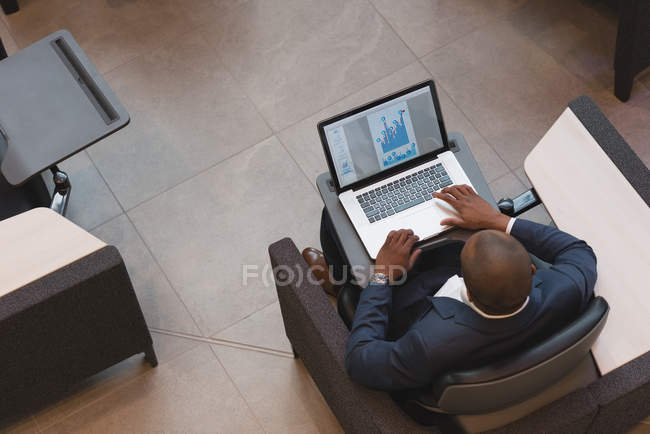 Vista superior del hombre de negocios usando el ordenador portátil sentado en el vestíbulo en la oficina moderna - foto de stock