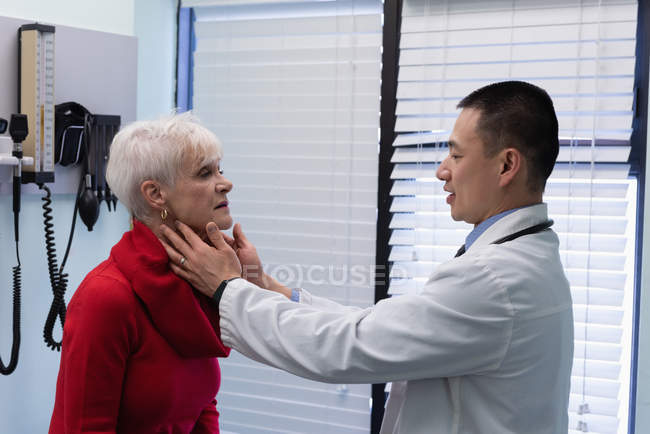 Seitenansicht eines jungen asiatischen Arztes, der mit einem älteren Patienten in der Klinik interagiert — Stockfoto