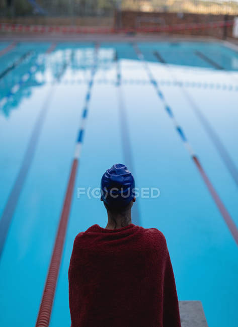 Rear view of young female swimmer wrapped in towel standing near swimming pool — Stock Photo